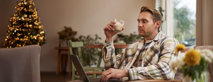 Handsome blond man with laptop, sitting in cafe and drinking coffee, working online, freelancing, set up workspace outside of an office environment.