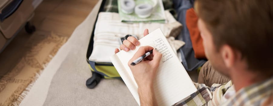 Close up portrait of man packing suitcase, making notes, check-list of items he wants to take on holiday, packing luggage.