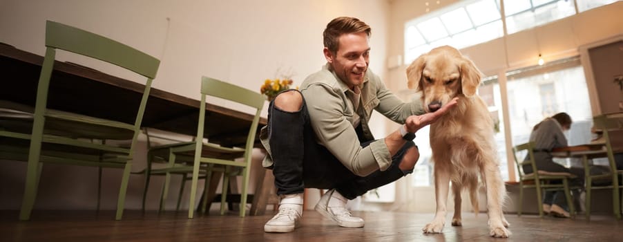 Close up portrait of happy dog owner, man with his pet giving a treat, spending time in animal-friendly cafe or co-working space.