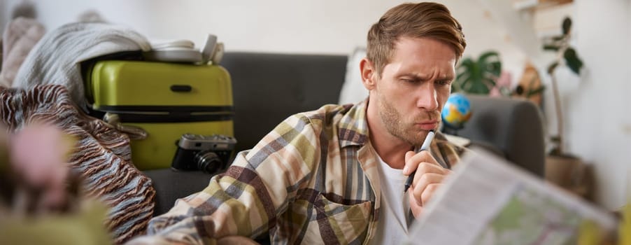 Man with confused face reads the map, traveller plans holiday, looks puzzled. Tourism concept