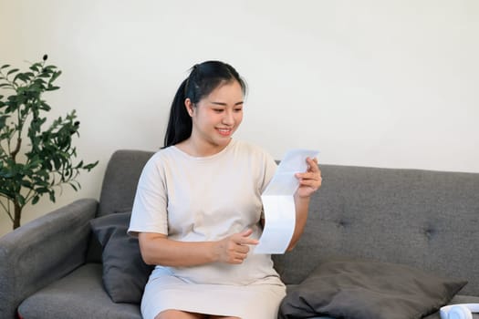 Pregnant woman admiring ultrasound pictures, gently touching her baby bump.