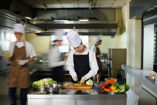 Chef apprentice working on vegetable preparation in a busy kitchen..
