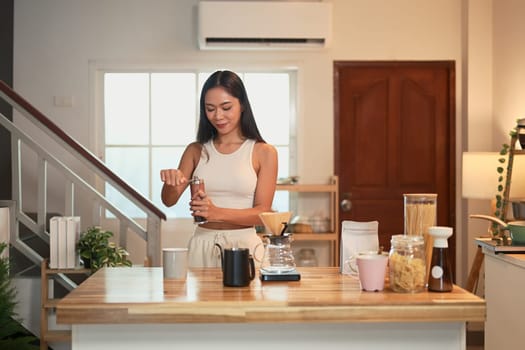 Beautiful woman grinding coffee beans in a kitchen, preparing fresh pour over coffee.