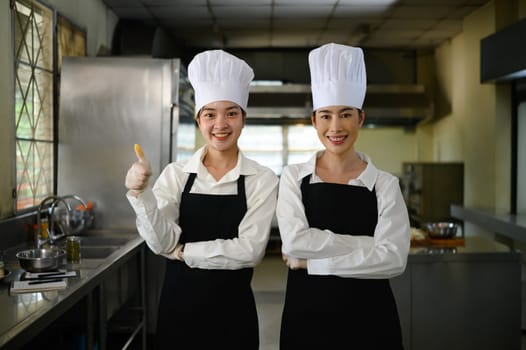 Confident culinary students in professional chef uniforms pose proudly in the kitchen.