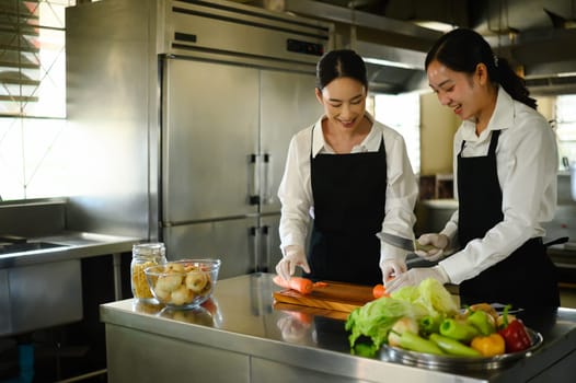 Two female culinary students preparing vegetables during a cooking class in a professional kitchen.