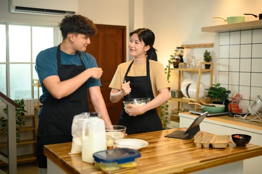 Man and woman wearing aprons mixing ingredients for pancakes in a cozy kitchen.