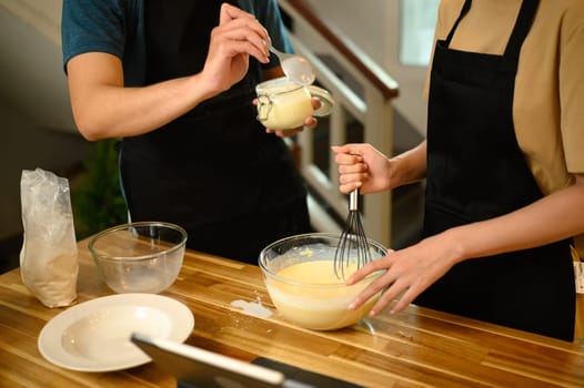 Man and woman wearing aprons mixing ingredients for pancakes in a cozy kitchen.