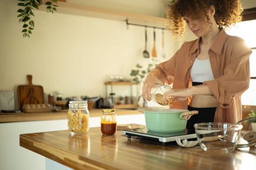 Young woman with curly haired preparing a meal in a bright home.