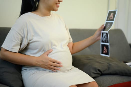 Pregnant woman admiring ultrasound pictures, gently touching her baby bump.