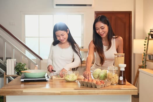 Young asian girl learning to cook with her mom in cozy home kitchen.
