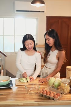 Young asian girl learning to cook with her mom in cozy home kitchen.