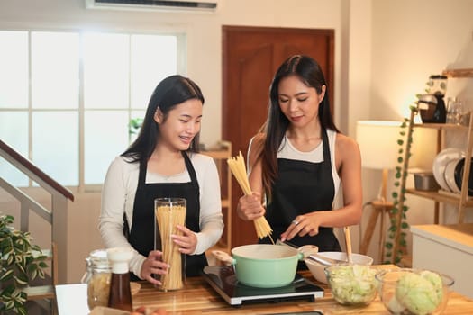 Smiling mother and teenage daughter preparing spaghetti at home.