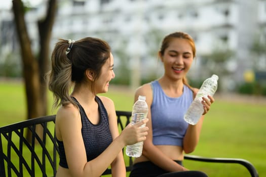 Two cheerful female friends cooling down with bottled water after a workout.