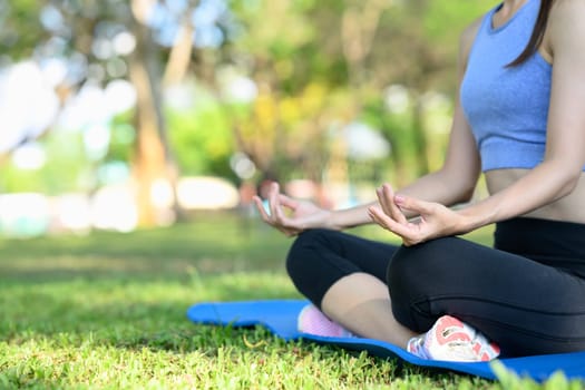 Close-up of a woman in lotus position meditating on a yoga mat in a peaceful park.