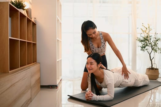 Mother guiding teenage daughter in plank exercise on mat during home workout session.