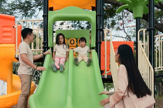 Parents watching and guiding their children as they play on a slide at the playground.