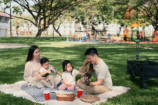 Parents and two children sharing a joyful outdoor meal during a weekend picnic in a green park.