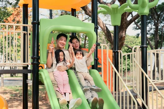 Happy family of four sliding together at a playground.