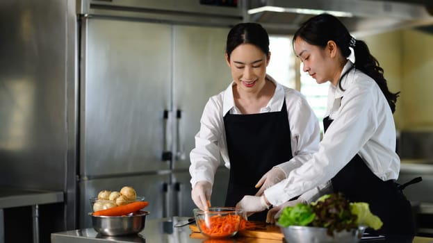 Two female culinary students preparing vegetables during a cooking class in a professional kitchen.
