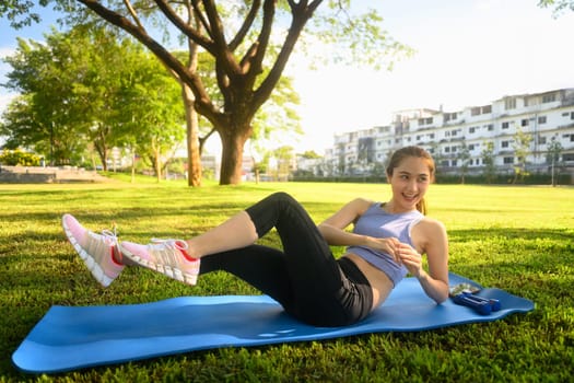 Young woman doing abdominal exercises on a yoga mat in the park.