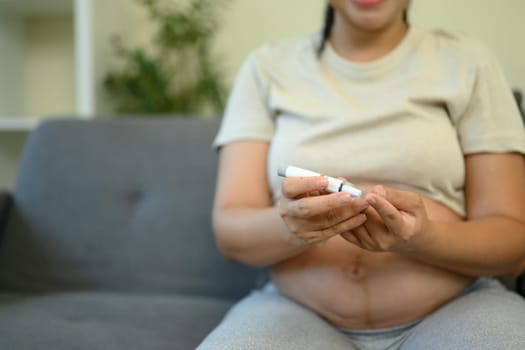 Pregnant woman checking her blood sugar level with a glucometer at home.