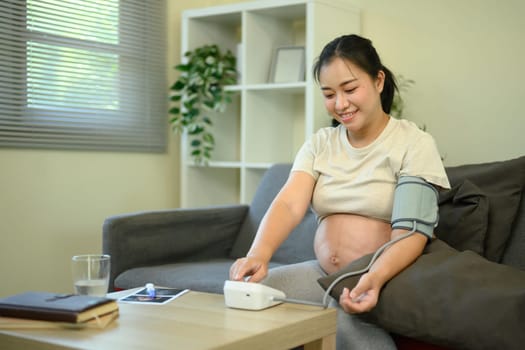 Expectant mother using digital blood pressure monitor to track her health during pregnancy.
