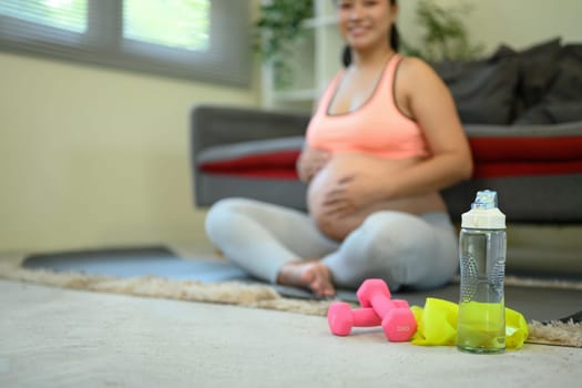 Pregnant woman sitting on the floor with a bottle of water and two dumbbells in front of her.