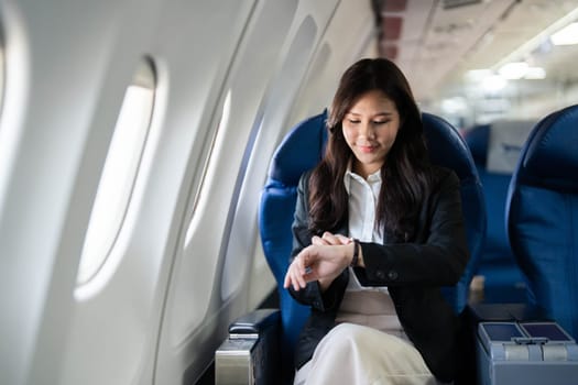 A young businesswoman checking her watch while seated on an airplane, reflecting on time management during her travels.