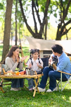 Parents and daughter camping in a forest park surrounded by nature and fresh food.