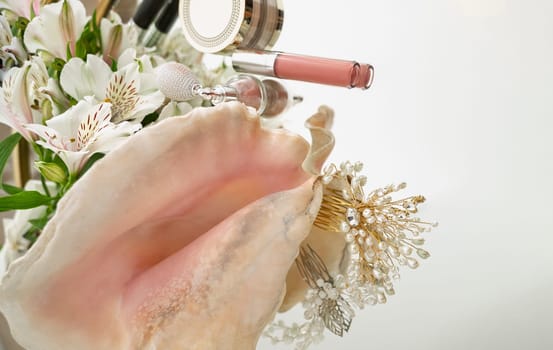 Lip gloss, highlighter, powder, flowers, hair ornaments with pearls, makeup brush, big seashell on mirror background. flat lay with space for text. horizontal photo