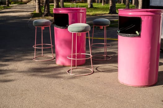 street cafe with tables made of iron barrels, bright pink color. high chairs near a pink barrel in the park.