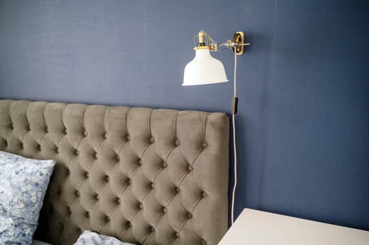 Modern upholstered headboard close-up with pillows in cozy bedroom. White pendant lamp and gray headboard, cozy minimalist bedroom. High quality photo