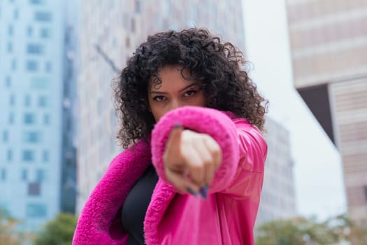 Graceful dancer with curly hair wearing a pink coat, expressing movement and energy in an urban environment. Modern fashion, contemporary dance, and artistic performance against a city backdrop.