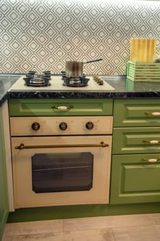 A saucepan on a gas stove in a kitchen interior. Green kitchen cabinets nearby.