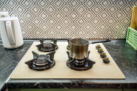 Close-up of a saucepan on a gas stove in a kitchen interior. Light beige gas panel, white electric kettle nearby.
