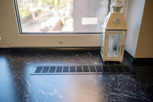 Plastic window, dark wood window sill and Christmas lantern. Interior detail, there is a white metal lantern on the window sill.