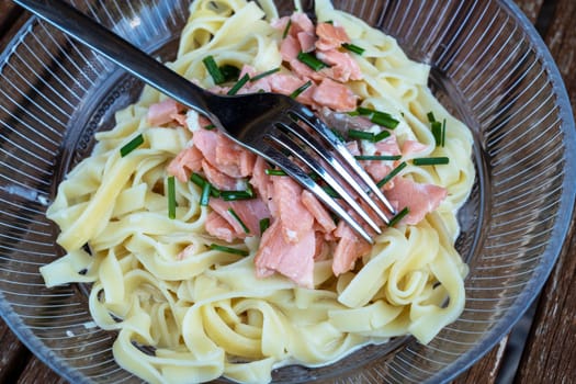 A fork is in a bowl of pasta with meat and green herbs. The pasta is white and the fork is silver