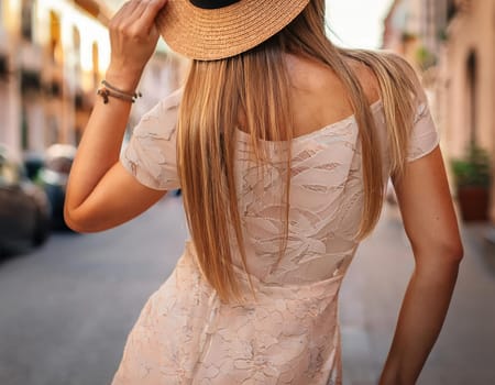 A woman wearing a straw hat and a white lace dress is standing on a street. The hat is tilted to the side, and the dress is flowing behind her. The scene has a casual and relaxed vibe. Generative AI