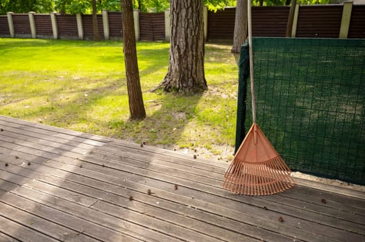 Close-up of an orange rake, with a park in the background. The park or yard is flooded with sun