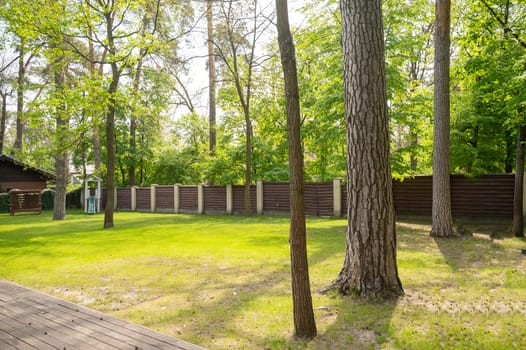 The courtyard has a lawn, large trees and grass. The courtyard is surrounded by a high brown fence.