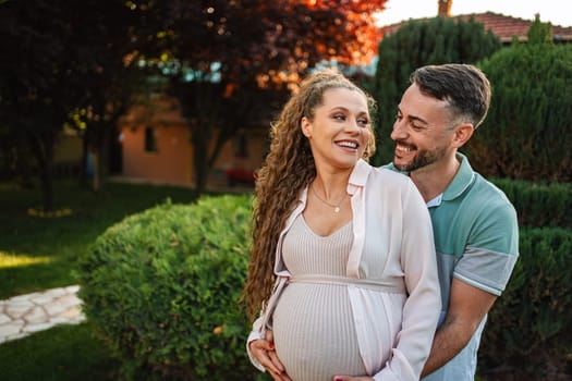 A couple embraces in a lush garden anticipating their baby.