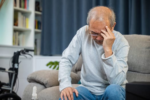 Asian mature old man sitting on sofa headache at home in living room, Depressed senior man unhappy hands rubbing eye suffering from a migraine. Health care