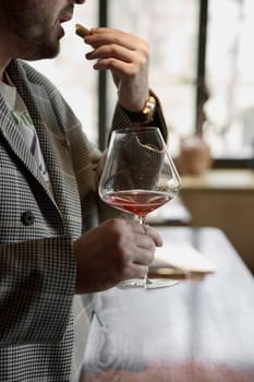 Champagne tasting in restaurant, A man holds in his hand a beautiful elegant glass with rose sparkling wine, He eats delicious snacks and drinks pink wine. High quality photo