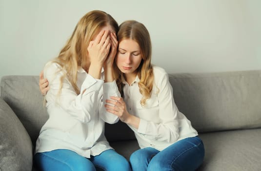 Upset offended caucasian two women, mature mother or sister and adult daughter crying together sitting on couch at home