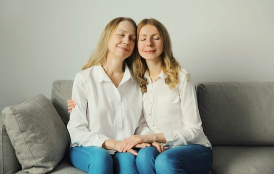 Portrait of happy two women, smiling mature mother and adult daughter together hugging sitting on couch in living room at home, warm family feelings