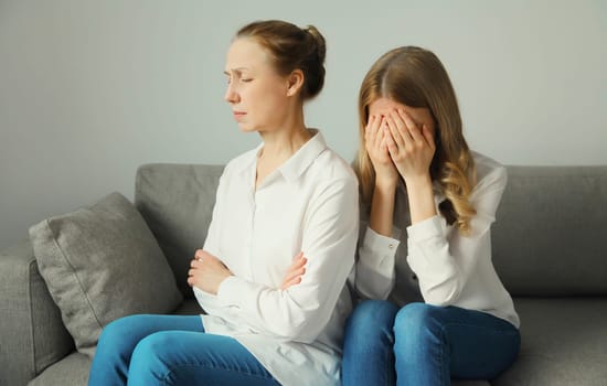 Upset offended caucasian two women, mature mother or sister and adult daughter crying together sitting on couch at home