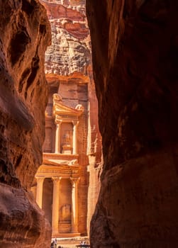 The carved facade of the Treasury building or Al-Khazneh in the ancient city of Petra in Jordan seen through narrow Siq gorge