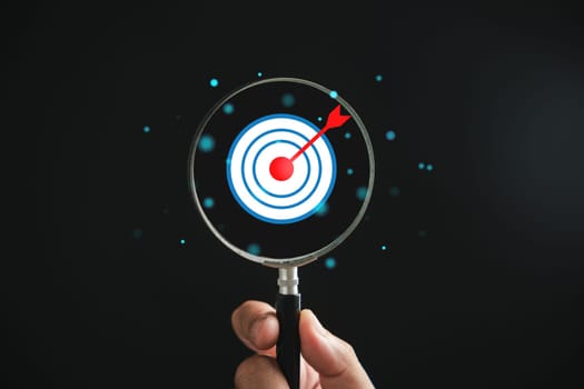 A magnifier glass highlights target board for focused business objectives, against a background with copy space. It represents the concepts of search, goal achievement, strategy, and marketing success