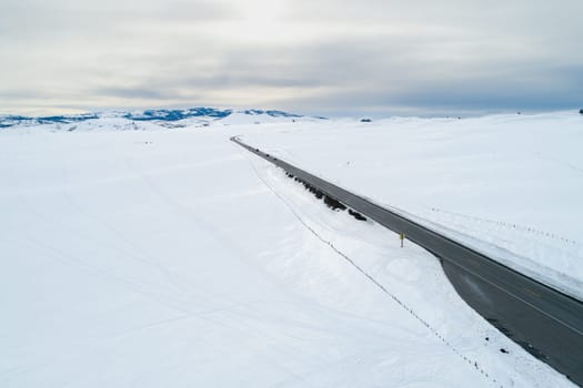 A road in the snow with a yellow sign on the side. The road is empty and the sky is cloudy