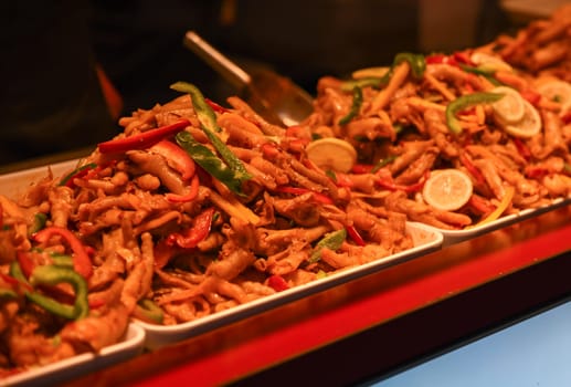 Spicy marinated chicken feet with lemon and chili peppers served in trays at a Shanghai street food market, traditional Chinese cuisine dish.